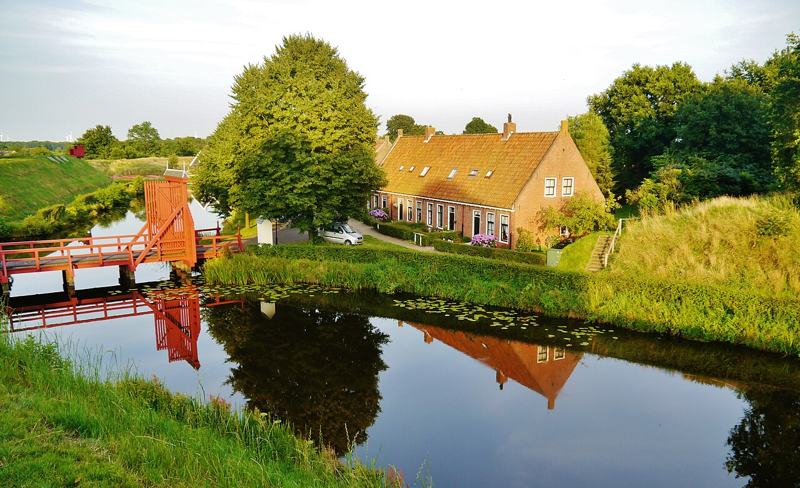 Festungsgraben mit roter Holzbrücke und Backsteinhaus in Bourtange